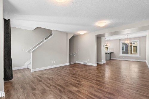 Unfurnished living room with wood finished floors, stairs, a textured ceiling, and a chandelier - 36 330 Bulyea Road, Edmonton, AB - Indoor