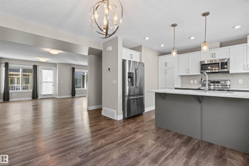 Kitchen with open floor plan, decorative backsplash, stainless steel appliances, white cabinets, and dark wood-style flooring - 36 330 Bulyea Road, Edmonton, AB - Indoor Photo Showing Kitchen With Stainless Steel Kitchen With Upgraded Kitchen