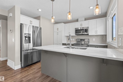 Kitchen with appliances with stainless steel finishes, backsplash, white cabinetry, dark wood-style floors, and pendant lighting - 36 330 Bulyea Road, Edmonton, AB - Indoor Photo Showing Kitchen With Stainless Steel Kitchen With Double Sink With Upgraded Kitchen