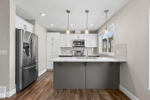 Kitchen featuring a peninsula, stainless steel appliances, white cabinetry, tasteful backsplash, and dark wood-type flooring - 36 330 Bulyea Road, Edmonton, AB - Indoor Photo Showing Kitchen With Upgraded Kitchen