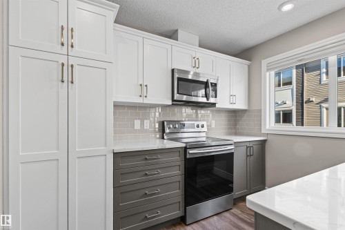 Kitchen featuring appliances with stainless steel finishes, decorative backsplash, gray cabinetry, white cabinetry, and a textured ceiling - 36 330 Bulyea Road, Edmonton, AB - Indoor Photo Showing Kitchen
