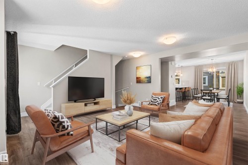 Living room featuring wood finished floors, a chandelier, a textured ceiling, and stairway - 36 330 Bulyea Road, Edmonton, AB - Indoor Photo Showing Living Room