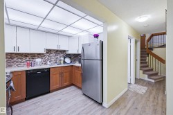 Kitchen featuring brown cabinetry, freestanding refrigerator, dishwasher, light wood-style flooring, and a textured ceiling - 