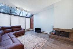 Living room featuring lofted ceiling, wood finished floors, a textured ceiling, a baseboard radiator, and a brick fireplace - 