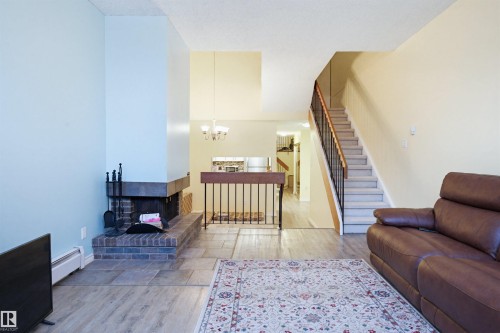 Living area with light wood-style floors, stairs, a baseboard radiator, a chandelier, and a brick fireplace - 11108 83 Avenue Nw, Edmonton, AB - Indoor Photo Showing Living Room