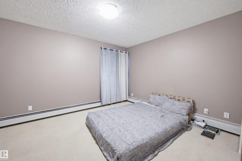 Carpeted bedroom with a textured ceiling and a baseboard heating unit - 11108 83 Avenue Nw, Edmonton, AB - Indoor Photo Showing Bedroom