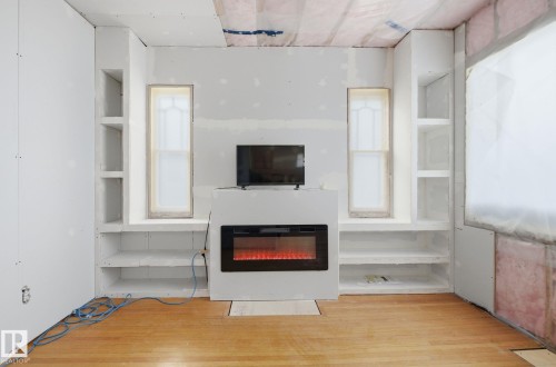 Unfurnished living room with built in features, light wood finished floors, and a glass covered fireplace - 11515 101 Street, Edmonton, AB - Indoor With Fireplace