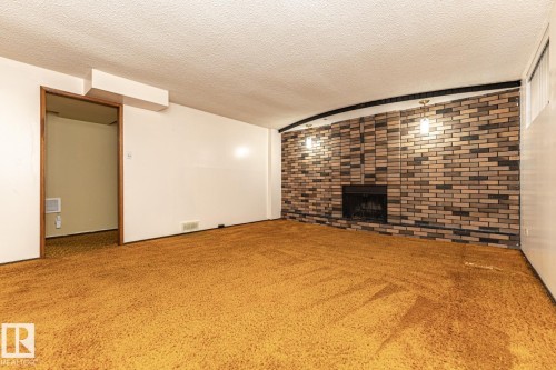 Unfurnished living room featuring a textured ceiling, a brick fireplace, carpet, and brick wall - 10207 165 Avenue, Edmonton, AB - Indoor With Fireplace