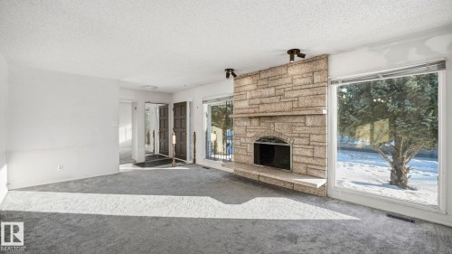 Unfurnished living room featuring a textured ceiling, carpet floors, and a fireplace - 10478 21 Avenue, Edmonton, AB - Indoor Photo Showing Living Room With Fireplace