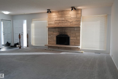 Unfurnished living room featuring a textured ceiling, a fireplace, and carpet floors - 10478 21 Avenue, Edmonton, AB - Indoor Photo Showing Other Room With Fireplace