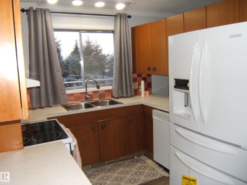 Kitchen featuring white appliances, light countertops, brown cabinets, backsplash, and extractor fan - 4910 53 Avenue, Willingdon, AB 