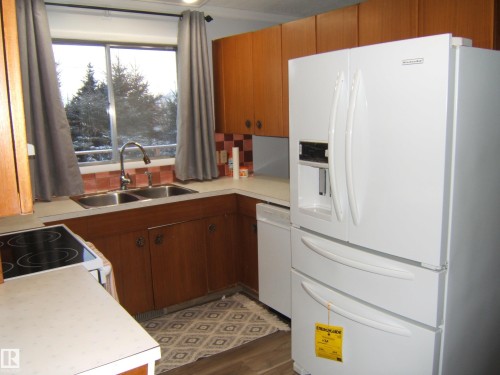 Kitchen with white appliances, light countertops, brown cabinets, dark wood-type flooring, and tasteful backsplash - 4910 53 Avenue, Willingdon, AB 