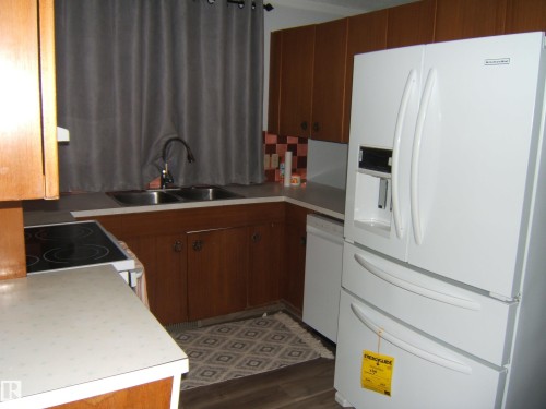 Kitchen with white appliances, light countertops, dark wood-type flooring, brown cabinetry, and backsplash - 4910 53 Avenue, Willingdon, AB 