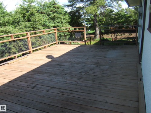 Expansive wooden deck with natural wood railing and wire mesh infill, surrounded by mature evergreen foliage - 4910 53 Avenue, Willingdon, AB 