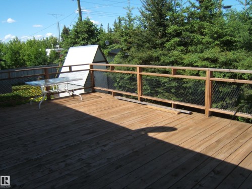 Expansive wood deck with wood and mesh railing, featuring surrounding mature trees - 4910 53 Avenue, Willingdon, AB 