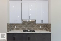 Kitchen with white cabinetry, light stone countertops, stainless steel gas cooktop, and under cabinet range hood - 