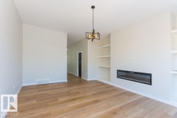 Unfurnished living room with built in features, light wood-type flooring, a glass covered fireplace, and a chandelier - 