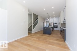 Kitchen with white cabinetry, decorative light fixtures, a kitchen island with sink, light wood-style floors, and appliances with stainless steel finishes - 