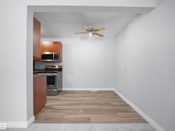 Kitchen with brown cabinetry, appliances with stainless steel finishes, light wood-style floors, dark countertops, and ceiling fan - 
