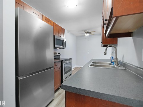 Kitchen with appliances with stainless steel finishes, brown cabinetry, dark countertops, light wood-style floors, and ceiling fan - 1460 Lakewood Road W, Edmonton, AB - Indoor Photo Showing Kitchen With Double Sink