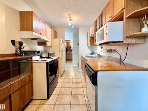 Kitchen featuring white appliances, a textured ceiling, under cabinet range hood, track lighting, and open shelves - 503 9737 112 Street, Edmonton, AB - Indoor Photo Showing Kitchen