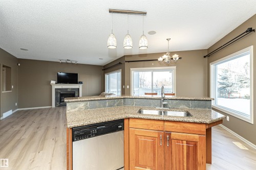 Kitchen with hanging light fixtures, track lighting, stainless steel dishwasher, an island with sink, and brown cabinetry - 1612 Lacombe Crest, Edmonton, AB - Indoor Photo Showing Kitchen With Double Sink