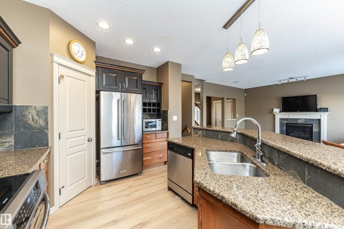 Kitchen featuring stainless steel appliances, hanging light fixtures, a textured ceiling, light stone counters, and a high end fireplace - 1612 Lacombe Crest, Edmonton, AB - Indoor Photo Showing Kitchen With Double Sink With Upgraded Kitchen