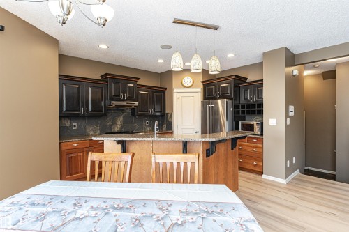 Kitchen with stainless steel appliances, a breakfast bar area, light stone counters, light wood finished floors, and decorative light fixtures - 1612 Lacombe Crest, Edmonton, AB - Indoor