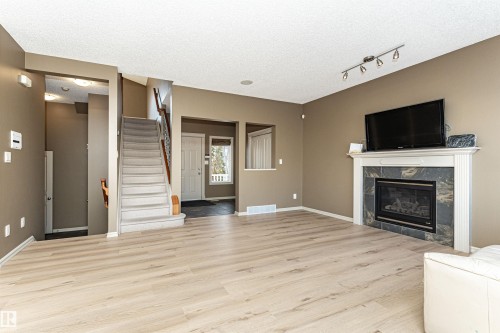 Unfurnished living room with a textured ceiling, stairway, a fireplace, light wood-style floors, and rail lighting - 1612 Lacombe Crest, Edmonton, AB - Indoor Photo Showing Living Room With Fireplace