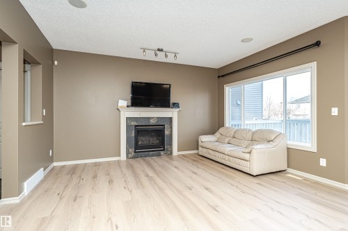 Living area featuring light wood-style floors, a tiled fireplace, a textured ceiling, and track lighting - 1612 Lacombe Crest, Edmonton, AB - Indoor Photo Showing Living Room With Fireplace