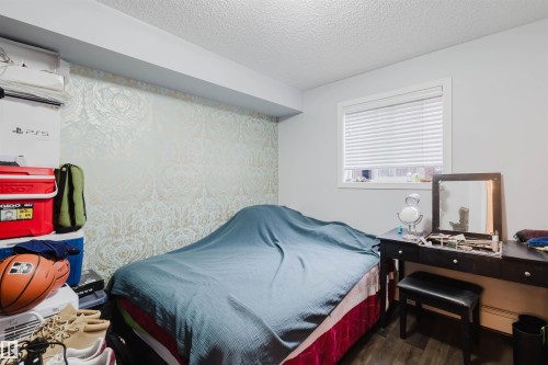 Bedroom with a textured ceiling, wood finished floors, a baseboard radiator, and a wall mounted air conditioner - 108 396 Silver Berry Road, Edmonton, AB - Indoor Photo Showing Bedroom