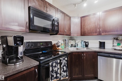 Kitchen with black appliances, a textured ceiling, dark countertops, dark brown cabinets, and track lighting - 108 396 Silver Berry Road, Edmonton, AB - Indoor Photo Showing Kitchen With Double Sink