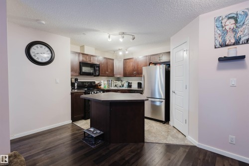 Kitchen featuring dark brown cabinetry, black appliances, a center island, dark wood-type flooring, and a textured ceiling - 108 396 Silver Berry Road, Edmonton, AB - Indoor Photo Showing Kitchen