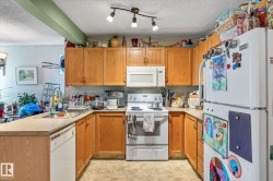 Kitchen featuring white appliances, a peninsula, a textured ceiling, light countertops, and brown cabinets - 