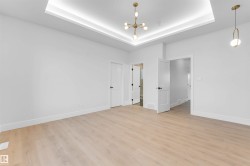 Unfurnished bedroom with a chandelier, light wood-style floors, and a tray ceiling - 