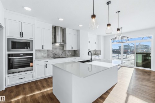 Kitchen with appliances with stainless steel finishes, decorative light fixtures, white cabinets, light stone countertops, and backsplash - 2211 4 Avenue, Edmonton, AB - Indoor Photo Showing Kitchen With Upgraded Kitchen