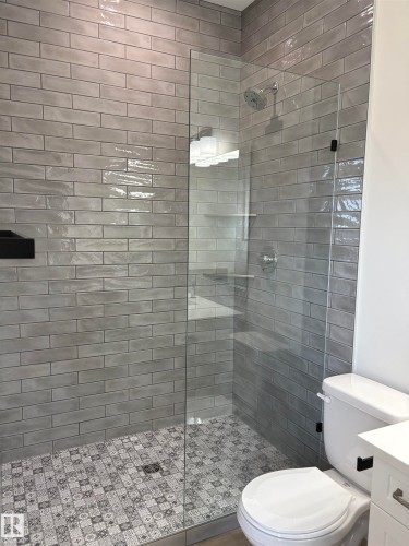 Tiled shower enclosure featuring a clear glass panel, gray subway wall tiles, and a patterned tile shower floor - 6 4 Avenue, Hay Lakes, AB 