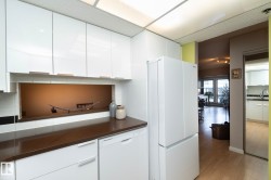 Kitchen featuring dark countertops, white cabinets, white appliances, backsplash, and light wood-style floors - 