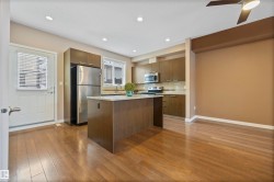 Kitchen with stainless steel appliances, a kitchen island, light stone countertops, dark wood-style floors, and modern cabinets - 