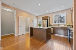 Kitchen with light stone countertops, appliances with stainless steel finishes, a kitchen island, a textured ceiling, and light wood-style flooring - 