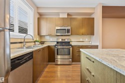 Kitchen featuring stainless steel appliances, light stone counters, dark wood-type flooring, backsplash, and modern cabinets - 