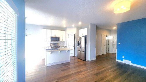 Kitchen with white cabinets, appliances with stainless steel finishes, an island with sink, dark wood finished floors, and light countertops - 4610 Kinsella Landing Sw, Edmonton, AB - Indoor Photo Showing Kitchen
