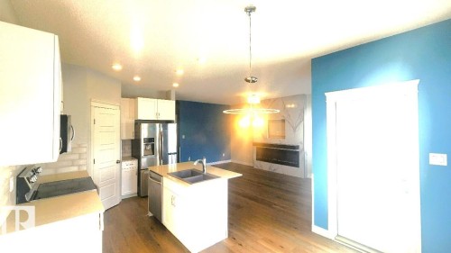 Kitchen featuring white cabinetry, hanging light fixtures, appliances with stainless steel finishes, a center island with sink, and dark wood-style floors - 4610 Kinsella Landing Sw, Edmonton, AB - Indoor Photo Showing Kitchen With Double Sink