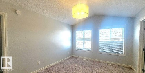 Carpeted spare room featuring a textured ceiling, lofted ceiling, and a smoke detector - 4610 Kinsella Landing Sw, Edmonton, AB - Indoor Photo Showing Other Room