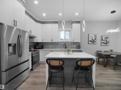 Kitchen featuring stainless steel appliances, hanging light fixtures, a kitchen island, white cabinets, and recessed lighting - 