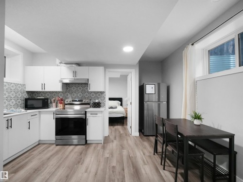 Kitchen with white cabinetry, stainless steel appliances, light countertops, light wood-style floors, and backsplash - 10911 159 Street, Edmonton, AB - Indoor Photo Showing Kitchen