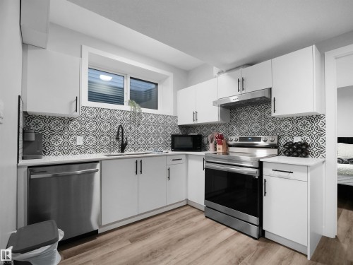 Kitchen featuring appliances with stainless steel finishes, white cabinetry, under cabinet range hood, light wood finished floors, and light stone counters - 10911 159 Street, Edmonton, AB - Indoor Photo Showing Kitchen With Upgraded Kitchen