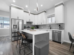 Kitchen featuring white cabinetry, stainless steel appliances, a kitchen bar, decorative light fixtures, and a kitchen island - 