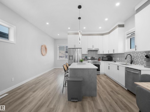 Kitchen featuring white cabinets, hanging light fixtures, appliances with stainless steel finishes, backsplash, and light stone counters - 10913 159 Street, Edmonton, AB - Indoor Photo Showing Kitchen With Upgraded Kitchen
