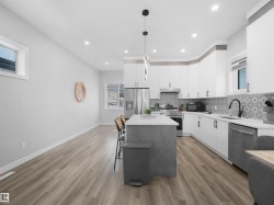 Kitchen featuring white cabinets, hanging light fixtures, appliances with stainless steel finishes, backsplash, and light stone counters - 